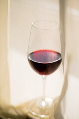 A glass of rich red wine catches the light through soft, flowing curtains, inviting relaxation