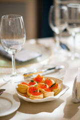 Canapés adorned with vibrant caviar rest on a white plate at a beautifully set table
