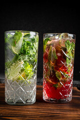 Two colorful cocktails with mint, lime, and fruit displayed on a rustic wooden surface