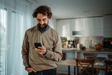 Man smiling using smartphone at home kitchen