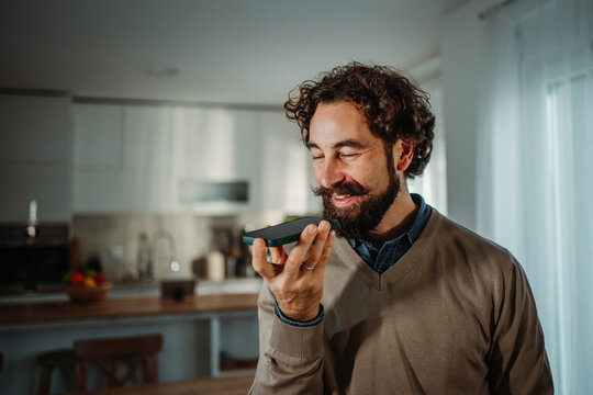 Man sending voice message on smartphone in kitchen