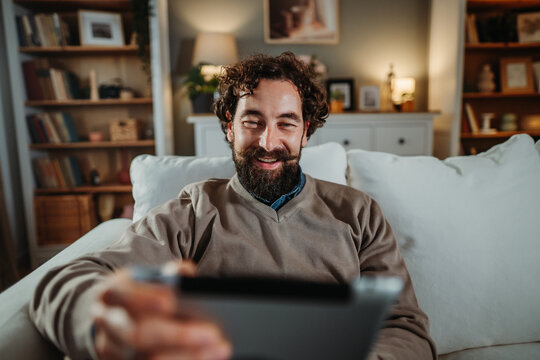 Smiling man relaxing on sofa using tablet at home