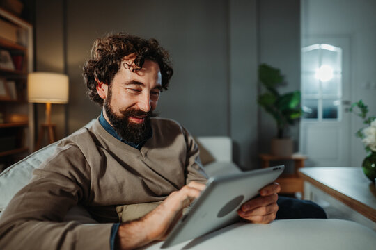 Man relaxing on sofa, using a digital tablet for entertainment