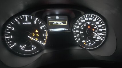 The dashboard of a vehicle displays various illuminated indicators, highlighting a low tire pressure warning as the engine is turned on. - Powered by Adobe