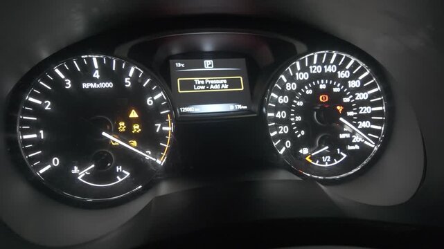 The dashboard of a vehicle displays various illuminated indicators, highlighting a low tire pressure warning as the engine is turned on.