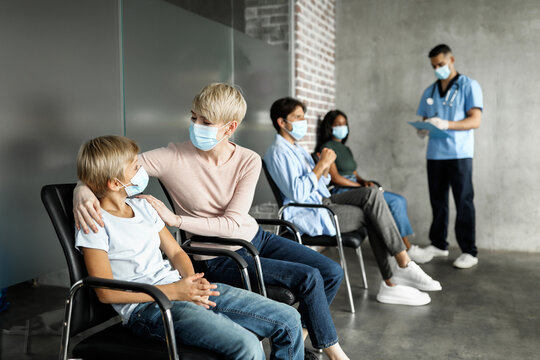 Mother comforting her son teen child, wearing protective face masks, getting vaccinated against COVID-19 at clinic. Kids, adults immunization while coronavirus pandemic concept, panorama