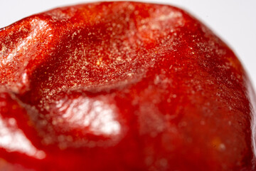 An extreme macro photograph capturing the intense red color, waxy texture, and subtle wrinkles on the surface of a chili pepper fruit, highlighting the stem base and granular res