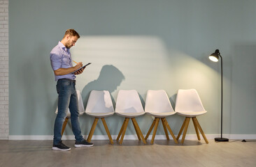 Busy man waiting for job interview in office lobby. Candidate for vacancy writing notes with pencil on clipboard for speech to recruiter, standing by chairs to check resume details and breathing