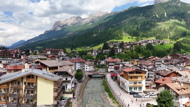 15 july 2024, Moena, Italy. Reveal flight, backwards drone flight above Avisio river in centre of Moena in Val di Fassa, beautiful Italian Dolomites during sunny summer day. Colorful houses. Beautiful