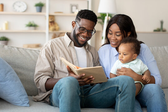 Caring young parents are bonding with their adorable infant son as they read to him on a comfortable couch. The family enjoys this relaxing moment together in their welcoming living room.