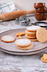 Shortbread cookies of round shape covered with sugar powder on the plate on the wooden table