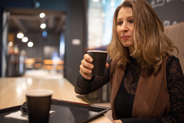 Smiling woman with long hair resting her head on her hand, enjoying a moment in a cozy cafe with warm lighting and a relaxed atmosphere, conveying happiness and contentment