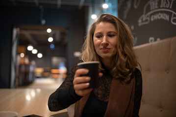 Smiling woman with long hair resting her head on her hand, enjoying a moment in a cozy cafe with warm lighting and a relaxed atmosphere, conveying happiness and contentment