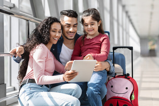 A family sits together in an airport terminal. They smile as they view a tablet, surrounded by their luggage. The atmosphere is warm and joyful, sharing a special moment.