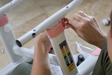 Close-up of woman’s hands assembling metal children’s furniture with electric screwdriver,...