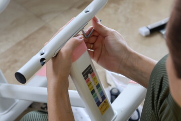 Female fingers gripping bolts and operating tools while assembling metal children’s furniture,...
