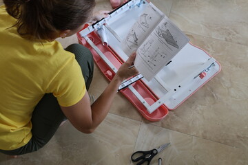 Woman assembling children’s furniture while checking instructions with screws, bolts and hardware parts spread around her