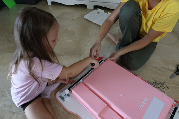 Mother and daughter working together on pink children’s furniture, metal and plastic pieces, hardware, screws, bolts and tools clearly visible
