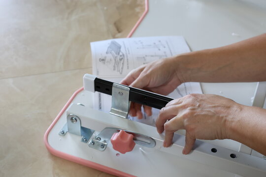 Close-up of female hands using tools and electric screwdriver assembling metal children’s furniture, holding bolts and screws