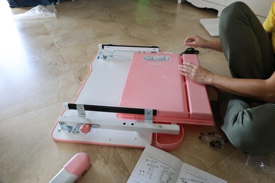 Woman on floor checking instruction sheet with metal furniture pieces, screws, bolts and scissors visible