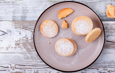 Shortbread cookies of round shape covered with sugar powder on the plate on the wooden table. Top view, copy space