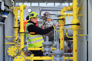 Gas pipeline technician adjusts pressure gauges and valves on industrial yellow piping, performing system calibration and safety checks at an energy facility.