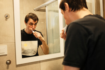 A man brushes his teeth while looking into the bathroom mirror. The moment represents personal hygiene and the concept of a healthy morning ritual.