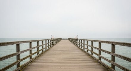 Obraz premium Empty wooden pier stretching into tranquil ocean under overcast sky