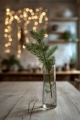 Fototapeta premium A tall glass vase with a single fir branch stands on a pale wooden table with faint festive lights in the distance.