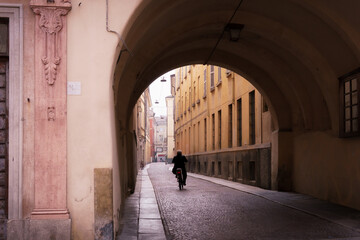 Quiet archway street in Parma Italy with lone cyclist on cobblestone road