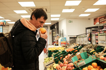 A man smells an orange to check its freshness. The moment reflects careful selection and mindful shopping.