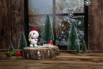  Snowman figurine with a red hat stands on a wooden stump surrounded by miniature Christmas trees,...