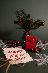A festive New Year composition featuring a handwritten “Happy New Year” note surrounded by red ornaments, berries, pine branches, and a small red gift box.