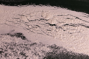 Close-up still-life of a scattered layer of flour on a dark green surface, showcasing its fine texture, soft shadows, and organic, natural pattern.
