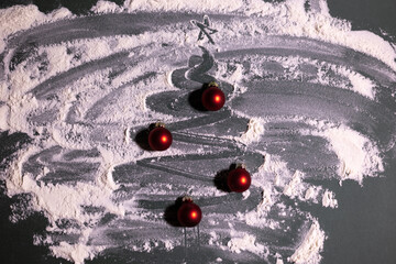 Creative Christmas-themed still-life featuring a tree shape drawn in scattered flour on a dark surface, decorated with small red baubles for a festive, handmade holiday look.