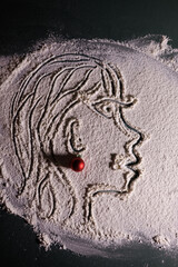 Artistic face illustration drawn in flour on a dark surface, accented with a small red Christmas ornament for a festive creative touch.