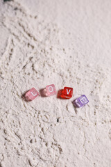 The word “LOVE” arranged from small cubes on a surface dusted with white flour, softly illuminated from the side by warm light, creating a cozy and delicate romantic atmosphere.
