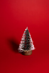 A small decorative Christmas tree with a wooden base, covered in white glitter, standing on a bright red background.