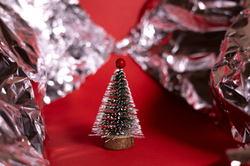 A small decorative Christmas tree with a wooden base, covered in white glitter, standing on a bright red background.