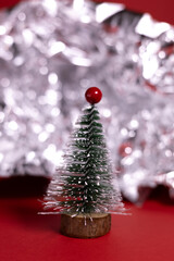 A small decorative Christmas tree with a wooden base, covered in white glitter, standing on a bright red background.
