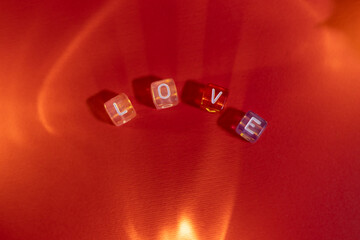 The word “LOVE” formed from small cubes on a red surface, illuminated by warm, soft lighting for a cozy and romantic atmosphere.
