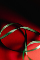 Close-up still-life of a green satin ribbon arranged in loose curves on a vivid red background, creating a festive, elegant, and minimal holiday-themed composition.