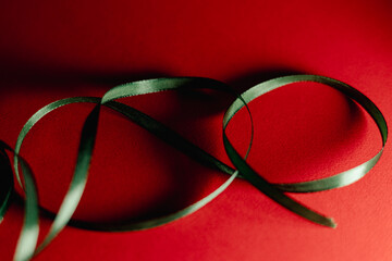 Close-up still-life of a green satin ribbon arranged in loose curves on a vivid red background, creating a festive, elegant, and minimal holiday-themed composition.