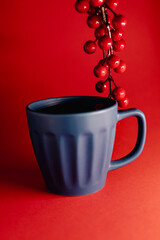 Festive still-life featuring a blue ceramic mug placed against a vibrant red background, accented with glossy red berries for a warm, seasonal holiday atmosphere.