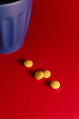 Close-up still life of several yellow tablets placed on a vibrant red surface next to a blue cup, creating a bold contrast and a clean, modern composition.