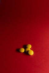 Close-up still life of several yellow tablets placed on a vibrant red surface.