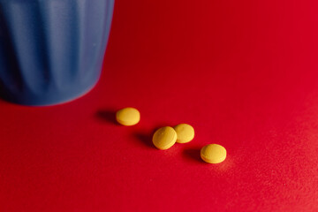 Close-up still life of several yellow tablets placed on a vibrant red surface next to a blue cup, creating a bold contrast and a clean, modern composition.