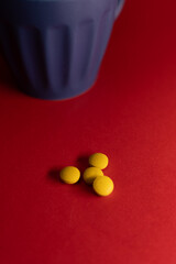 Close-up still life of several yellow tablets placed on a vibrant red surface next to a blue cup, creating a bold contrast and a clean, modern composition.