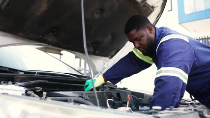 Local African mechanic in blue overalls and gloves works on a car engine at his workshop