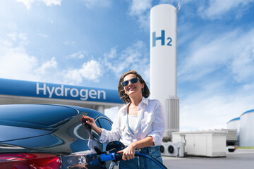 Obraz premium Woman holds a hydrogen fueling nozzle on a hydrogen filling station. Refueling car with hydrogen fuel